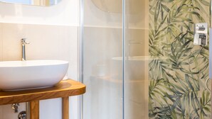 A bathroom with a white sink on a wooden countertop, a glass shower enclosure, and a wall with a leafy pattern. - Vittoria Rooms Sorrento (Sorrento)