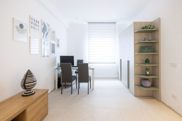 A modern, well-lit room with a dining area, a computer desk, and a bookshelf. - Vittoria Rooms Sorrento (Sorrento)