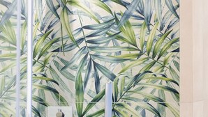 A bathroom with a shower head and a towel rack against a wall with a tropical leaf pattern. - Vittoria Rooms Sorrento (Sorrento)