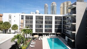 Un hotel moderno con piscina en la azotea, varios balcones y vistas a edificios altos aledaños.