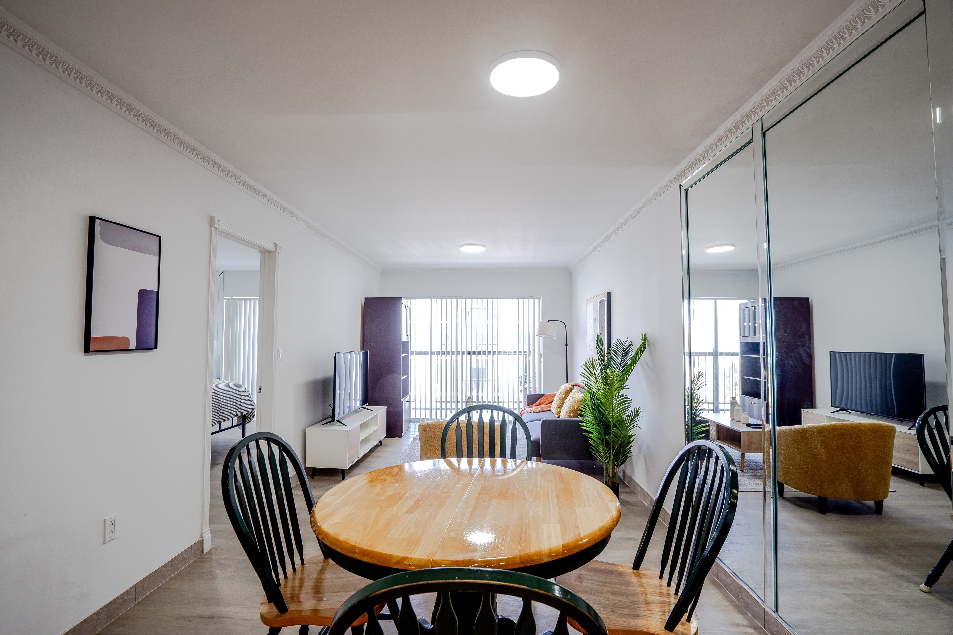 Een moderne woonkamer met een ronde houten eettafel, zwarte stoelen, een bank, een televisie en een groot raam.