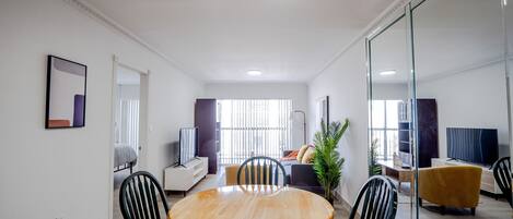 Een moderne woonkamer met een ronde houten eettafel, zwarte stoelen, een bank, een televisie en een groot raam.