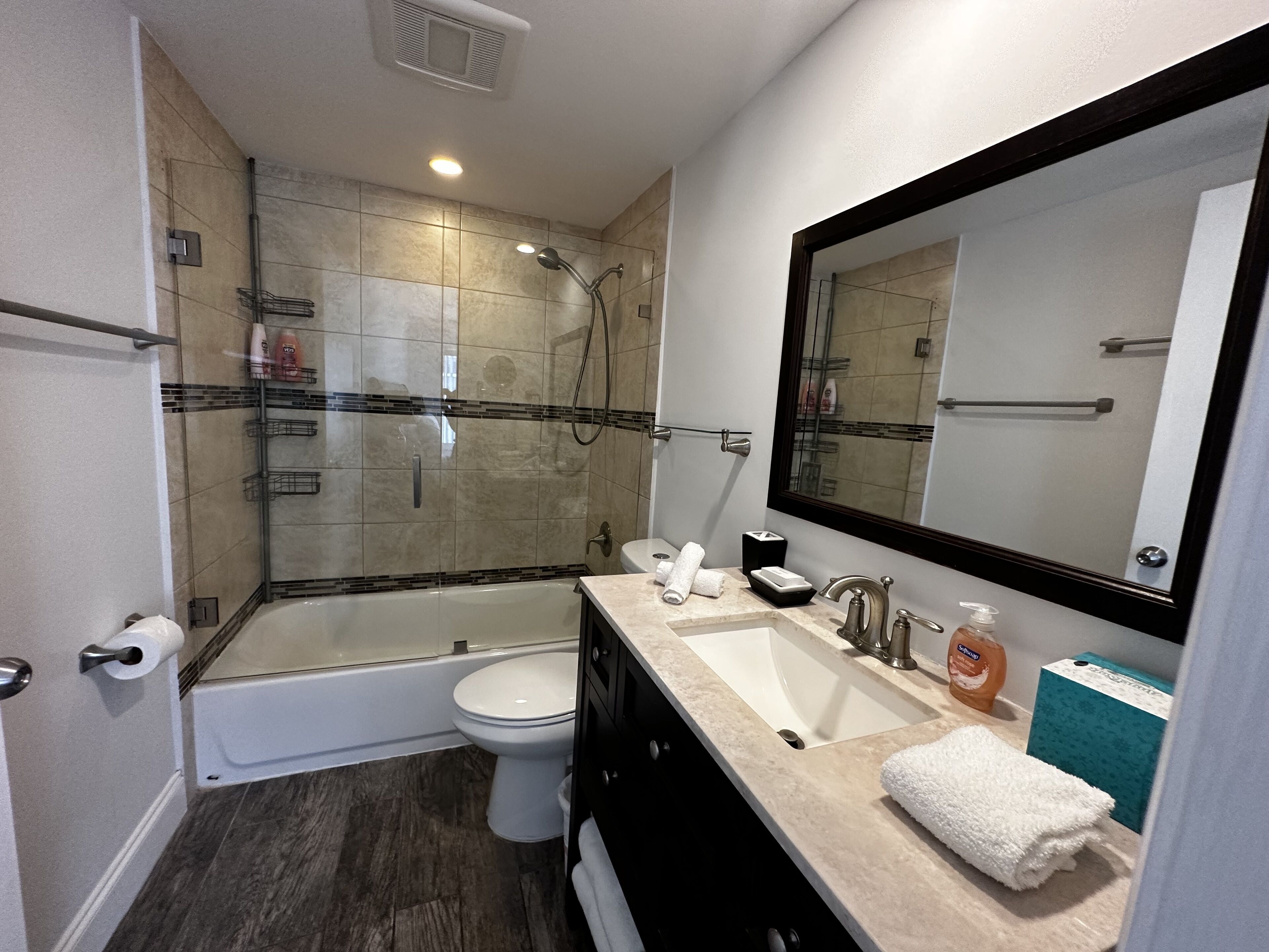 A modern bathroom with a glass-enclosed shower, a white toilet, a vanity with a sink, and a large mirror.