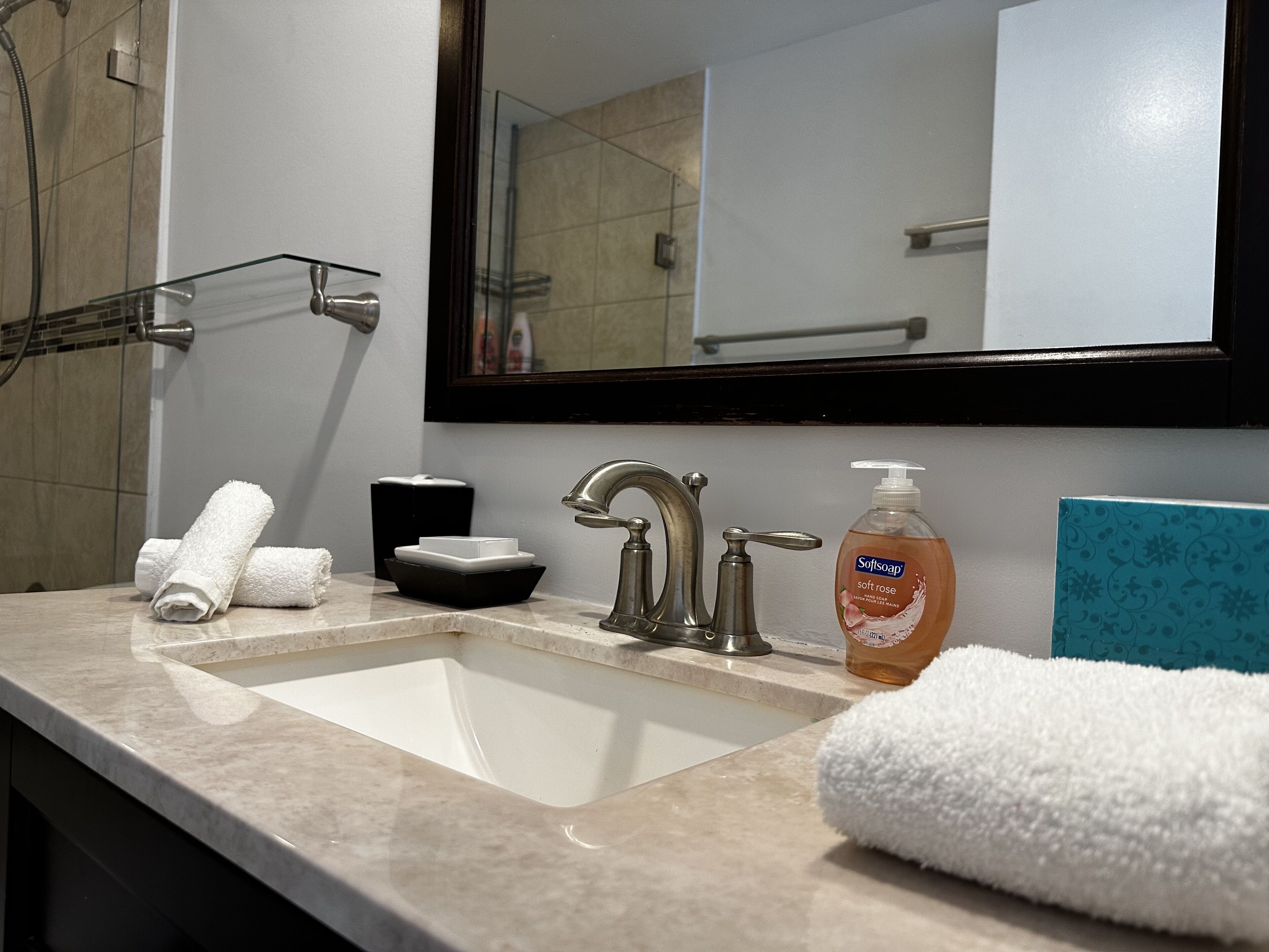 A bathroom with a sink, a mirror, a soap dispenser, and towels.