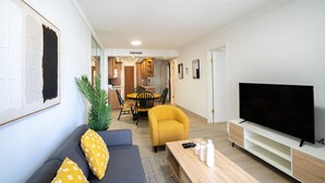 Una sala de estar con sofá, sillón, televisión y un comedor al fondo.
