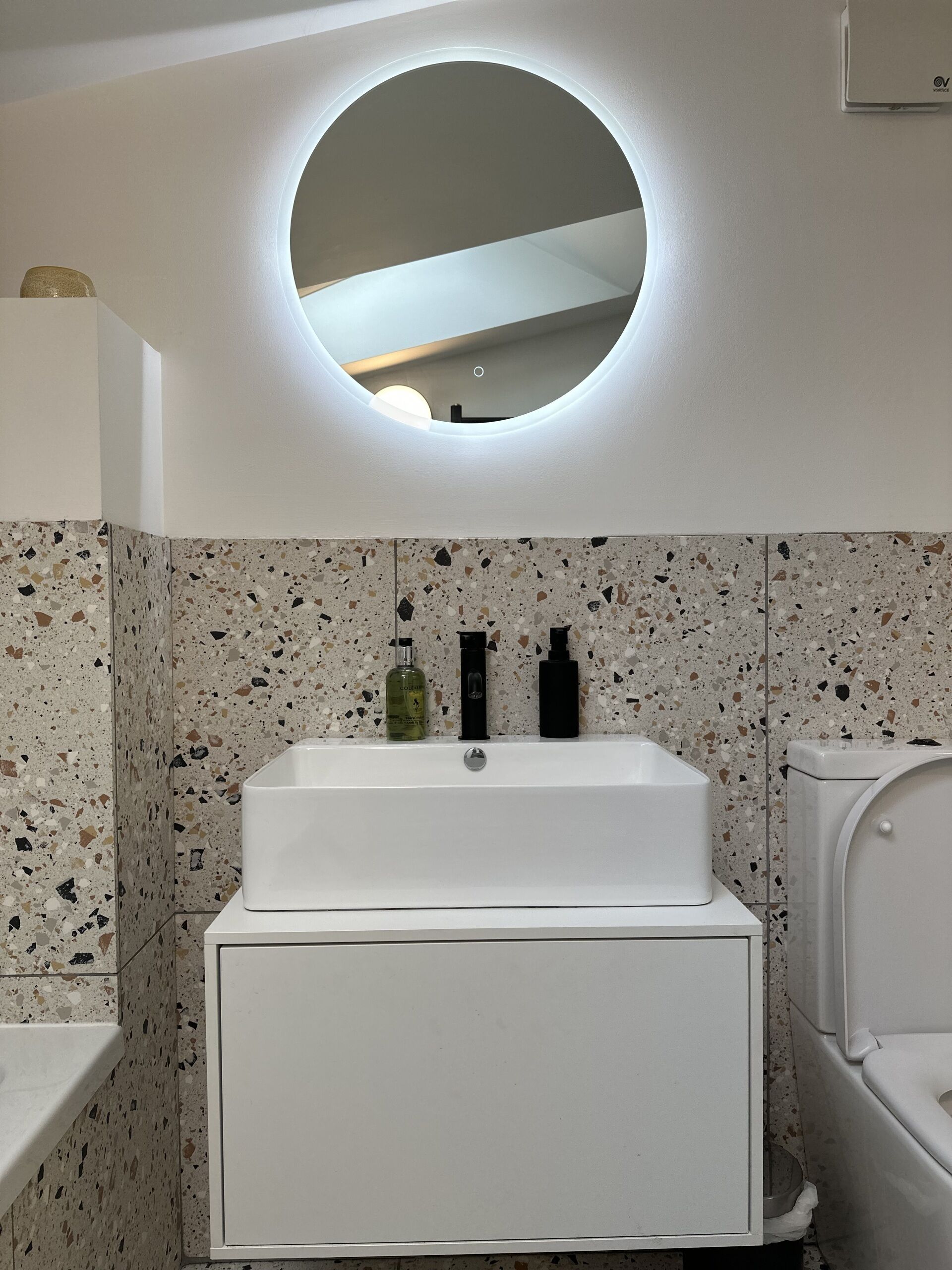 Un baño con un lavamanos blanco, un espejo redondo y un inodoro.