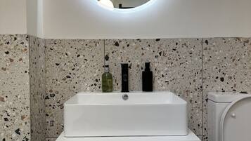 Un baño con un lavamanos blanco, un espejo redondo y un inodoro.