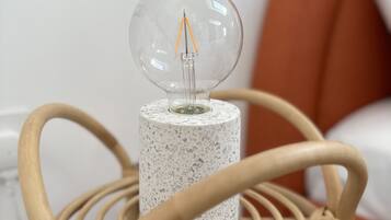 A clear glass light bulb on a speckled cylindrical base, placed on a woven chair with a white cushion in the background.
