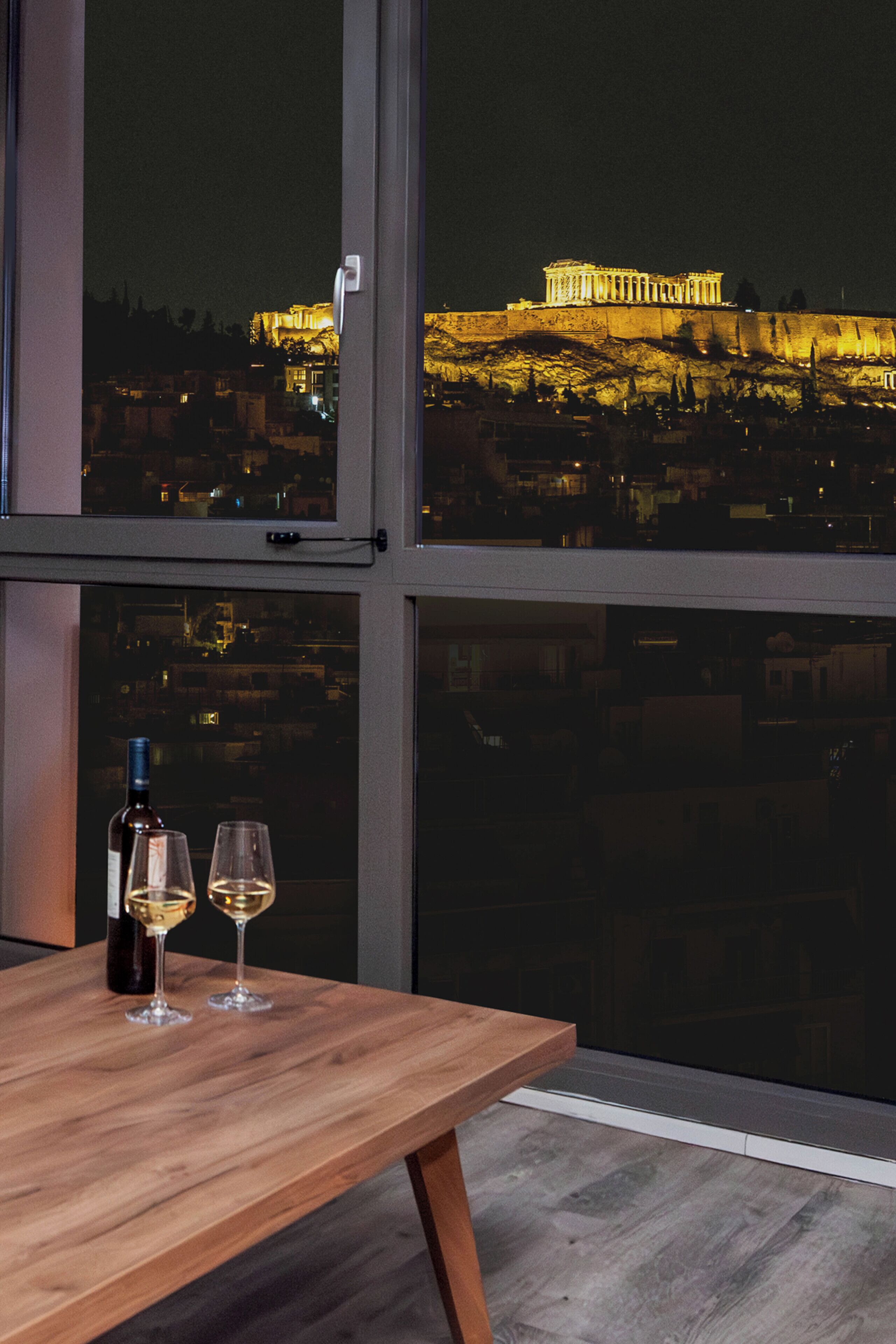 A table with two wine glasses and a bottle, overlooking a cityscape with illuminated buildings at night.