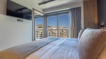 Habitación de hotel con una cama grande, un televisor de pantalla plana en la pared y vistas a la ciudad a través de amplios ventanales.