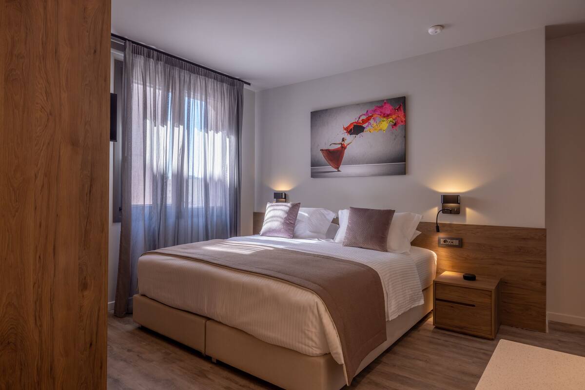 Une chambre à coucher moderne avec un grand lit, une tête de lit en bois et un tableau représentant une danseuse.