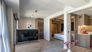 Un salón moderno con televisor de pantalla plana, suelo de madera, una mesa de comedor con un jarrón de flores y una zona de cocina con armarios de madera y un electrodoméstico rojo.