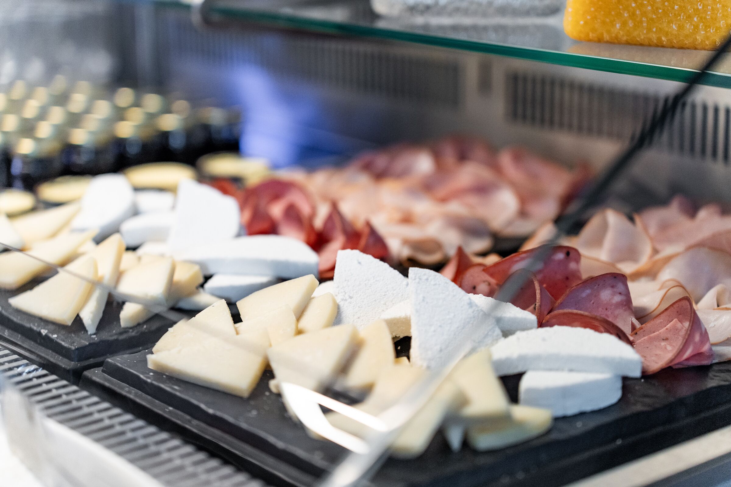 A variety of cheeses and cured meats displayed in a refrigerated case.