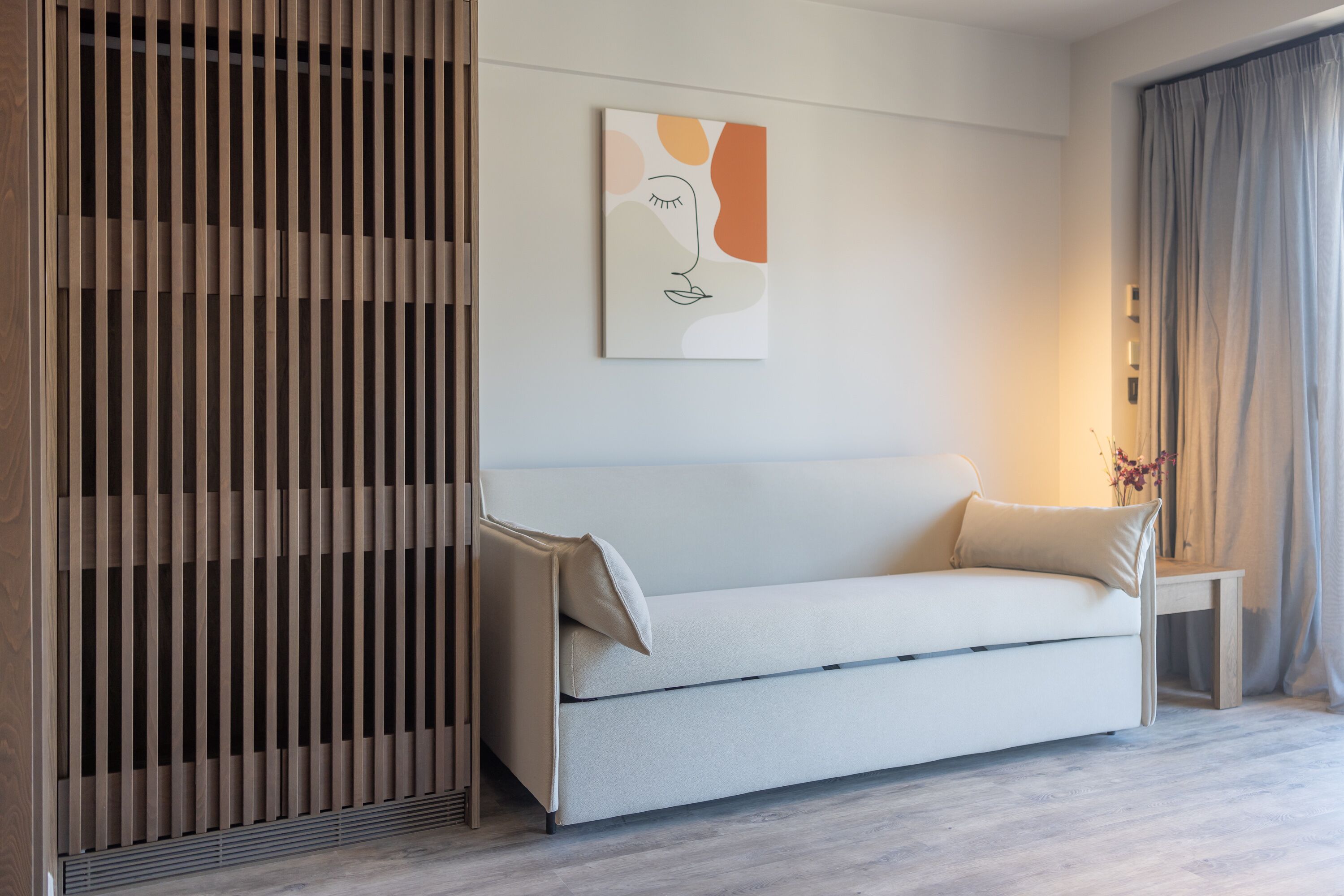 A modern living room with a white sofa, a wooden slat partition, and a minimalist artwork on the wall.