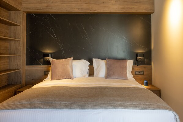 A modern bedroom with a large bed, wooden headboard, marble wall, and bedside lamps.
