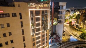 Un hotel de varios pisos con un llamativo letrero con el número '507', fachada de vidrio y una terraza en la azotea.