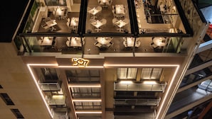 Un edificio de gran altura con restaurante en la azotea, que cuenta con varias mesas y sillas, el número '507' visible y un diseño arquitectónico moderno con barandales de vidrio.