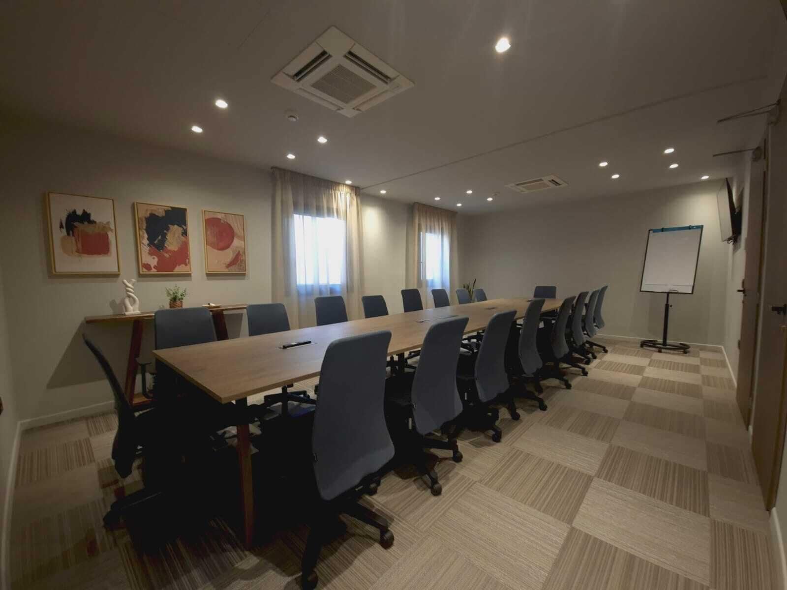 A conference room with a long table, multiple chairs, a whiteboard, and artwork on the walls.