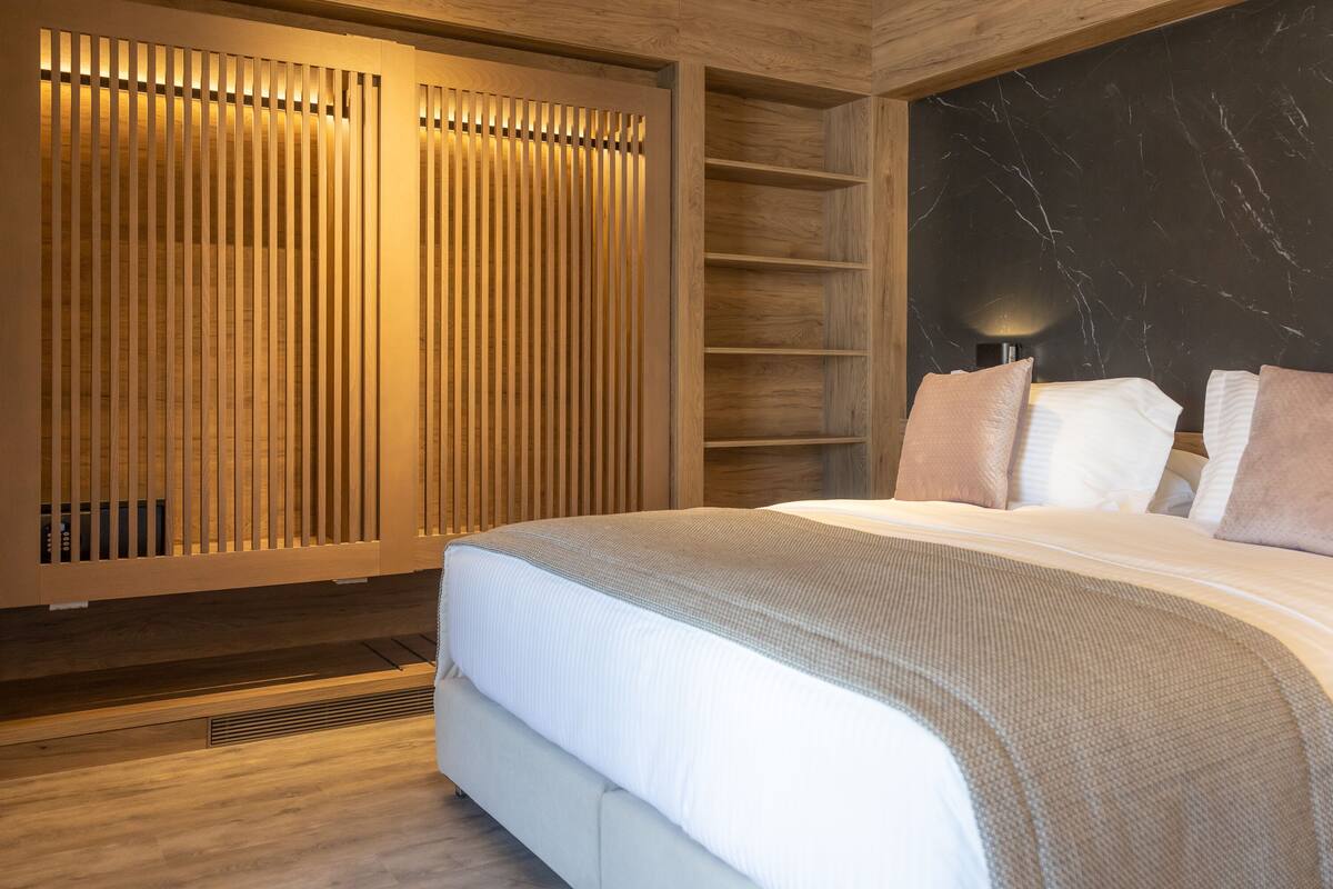 Une chambre moderne avec un grand lit, des stores en bois, un mur en marbre et une bibliothèque intégrée.