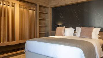 Un dormitorio moderno con una cama grande, paneles de madera, una pared de acento de mármol y una mesita de noche con lámpara.
