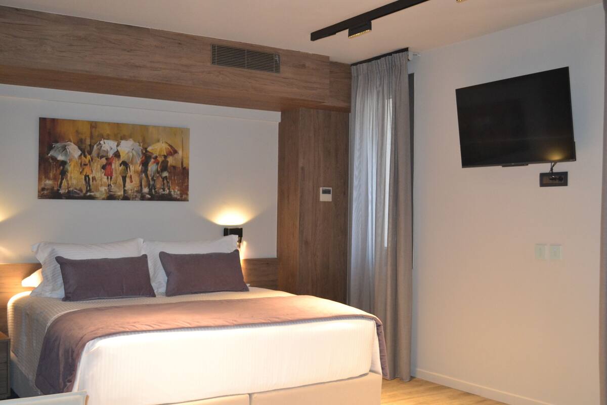 Une chambre d’hôtel moderne avec un grand lit, un tableau au mur, un téléviseur à écran plat et un plafond en bois.