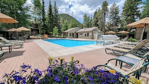 Zona de piscina con sillas de descanso y sombrillas, rodeada de árboles y con vista a una montaña.