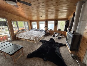 A cabin bedroom with a bed, a desk, a television, and a large window overlooking a lake. - 🏡 Welcome to our Private Oasis:  Spectacular 5-Bedroom Sandy Waterfront Home 🌞🏖️ (Powassan)