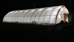 A large, white, semi-circular greenhouse structure with multiple windows and a ladder on the right side.