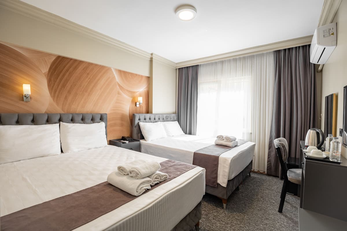 A hotel room with two beds, a desk, a chair, and a large window with curtains.
