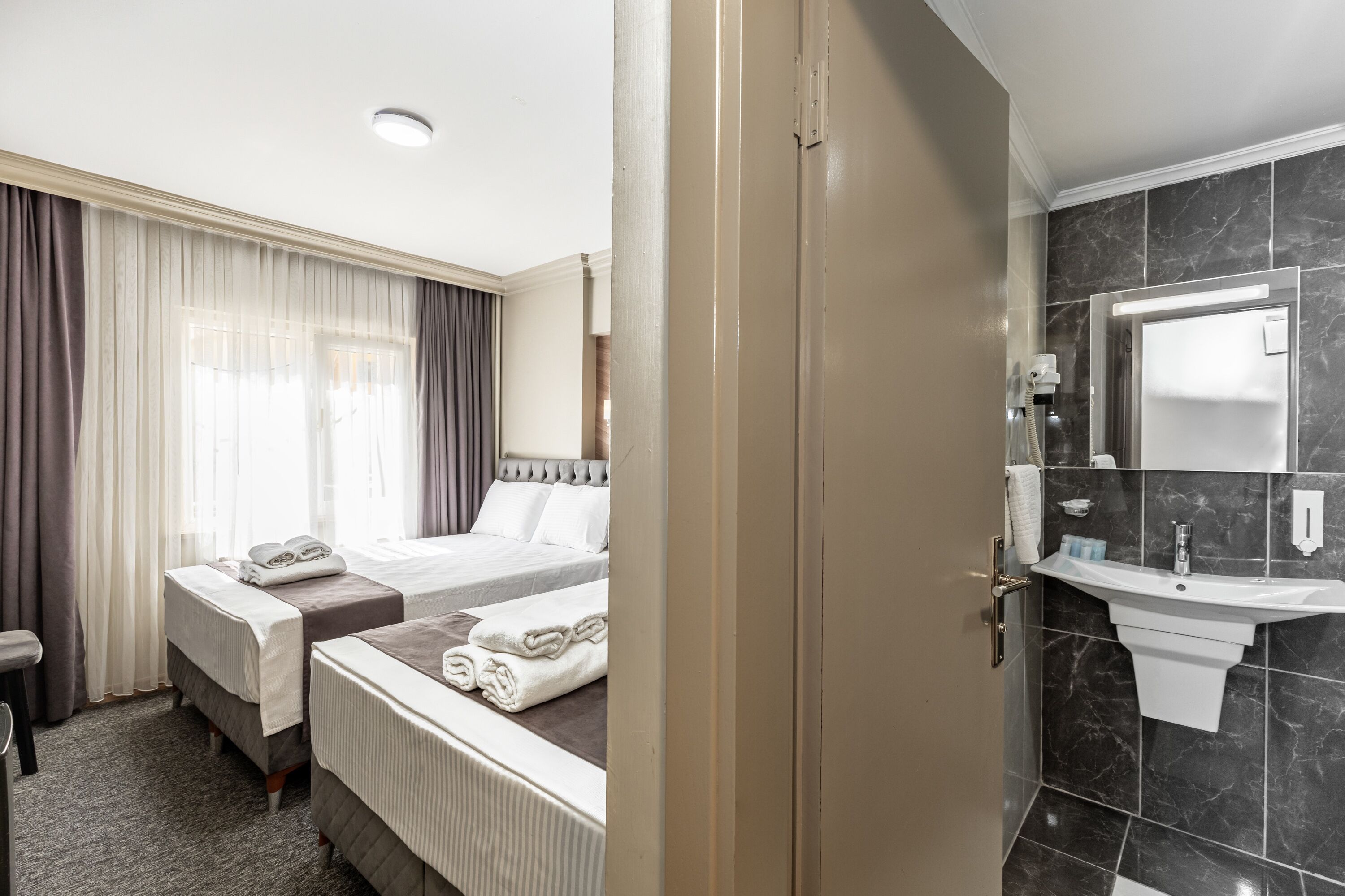 Une chambre d’hôtel avec deux lits, une salle de bain avec un lavabo et un grand miroir.