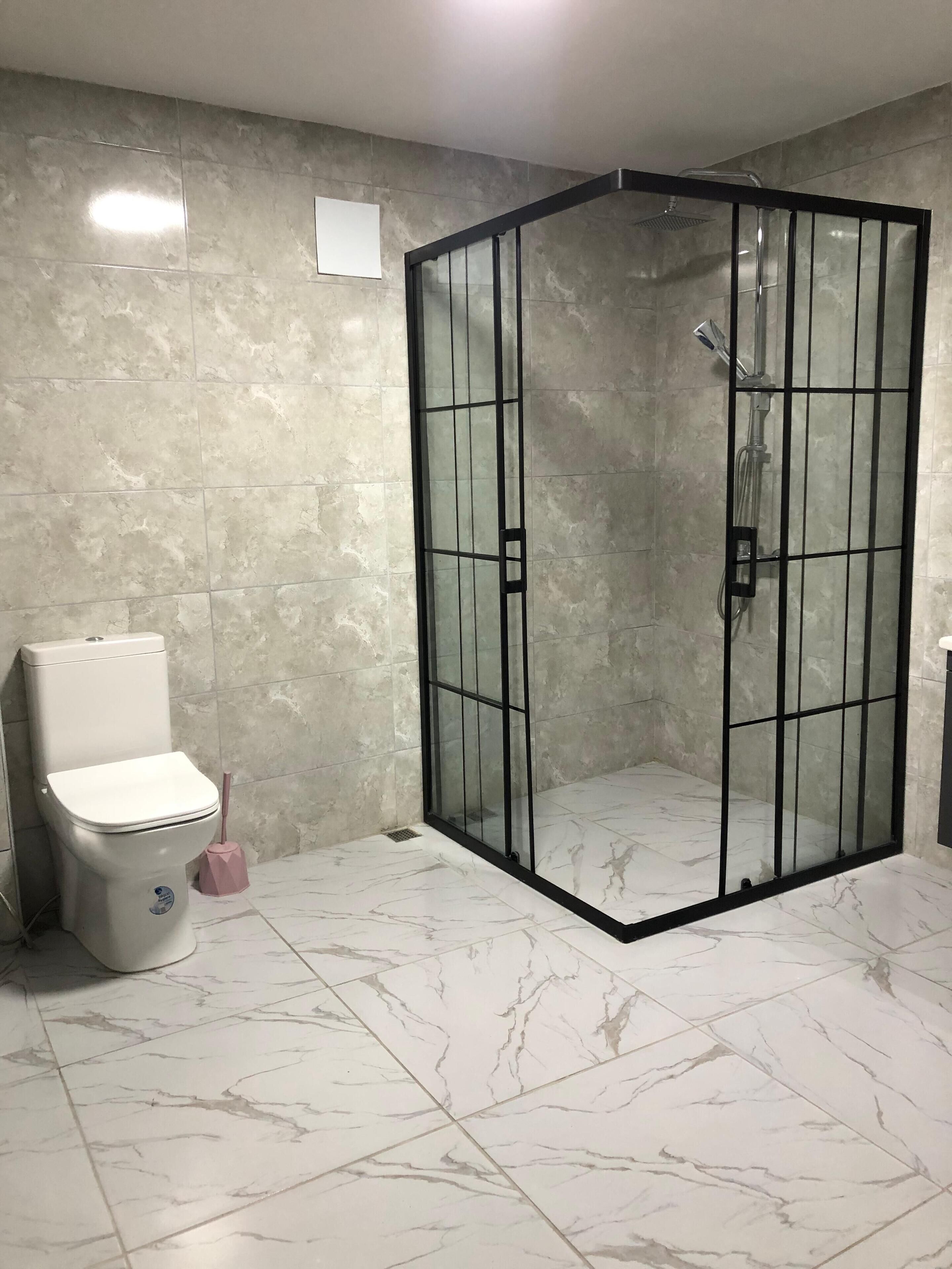 A bathroom with a glass-enclosed shower, a toilet, and a marble floor.