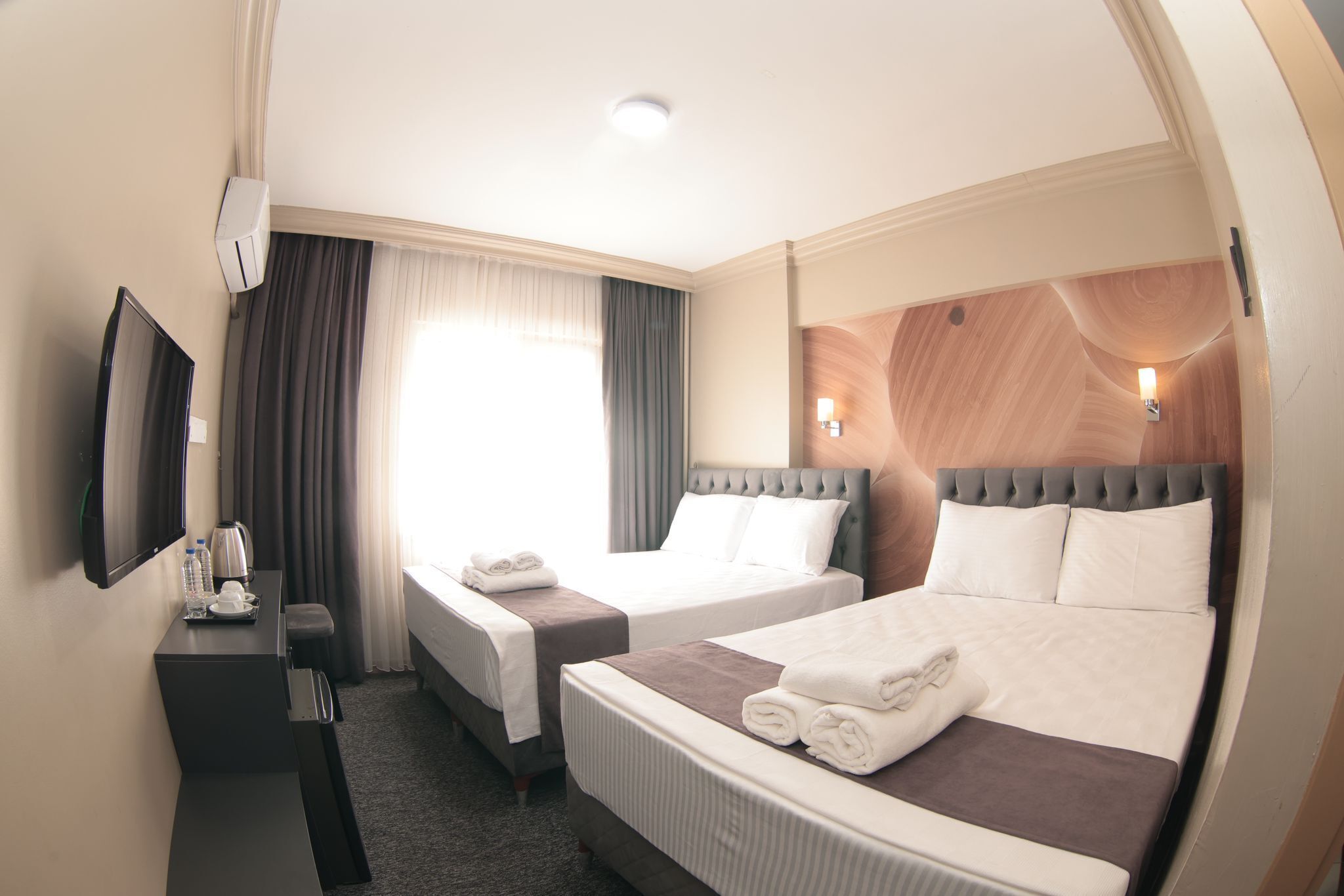 A hotel room with two beds, a desk, a flat-screen TV, and a window with curtains.