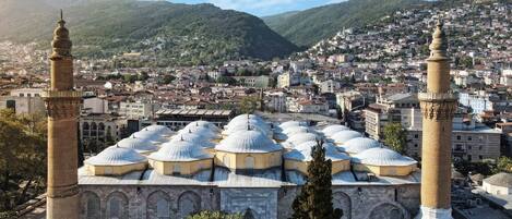 A historic building with multiple domes and minarets, surrounded by a mountainous landscape and a densely populated town.