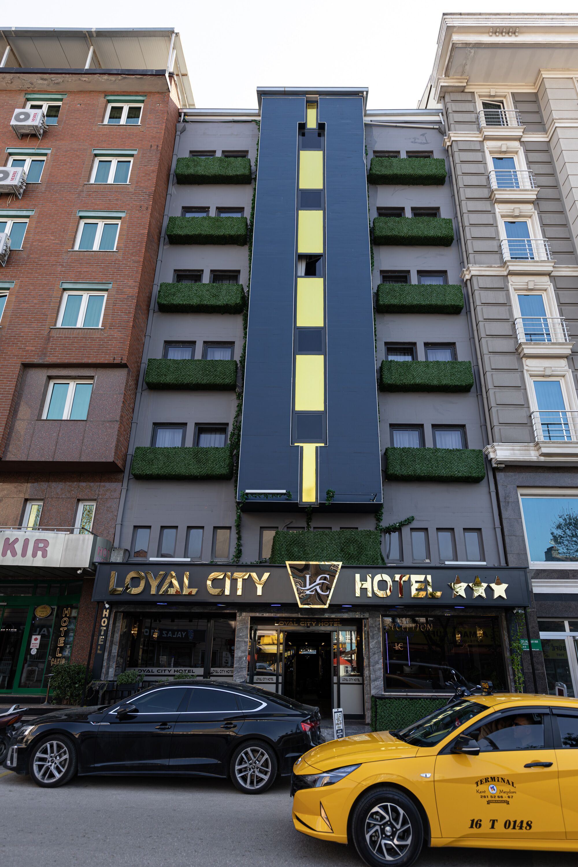 Un hotel con fachada moderna, que destaca por un diseño de franjas verticales y jardineras con plantas en los balcones.
