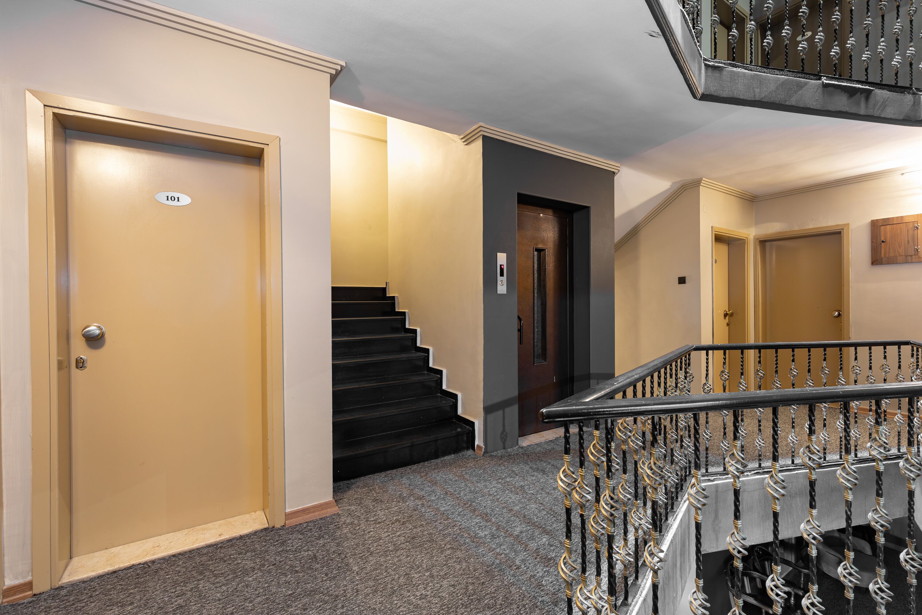 A hotel hallway with a carpeted floor, a staircase with a metal railing, and doors numbered 101 and 102.