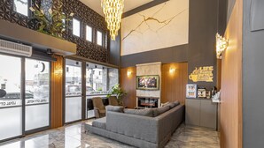 Un vestíbulo moderno con un sofá gris, detalles de madera, un televisor grande y un letrero que dice "LIFE BEGINS AFTER COFFEE".