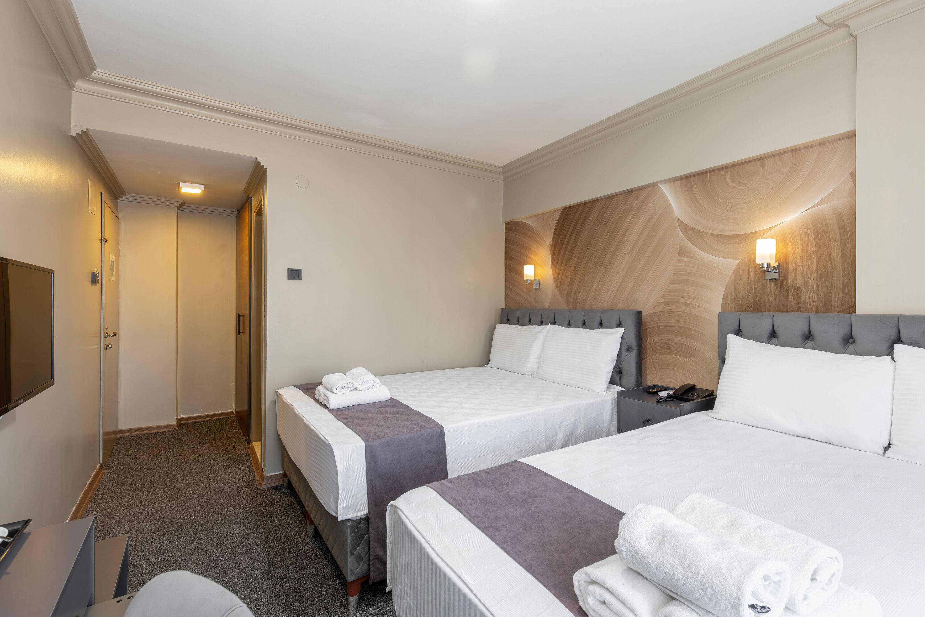 A hotel room with two beds, a desk, and a TV.