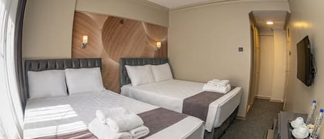 A hotel room with two beds, a flat-screen TV, a desk with a tray of toiletries, and a wooden accent wall.