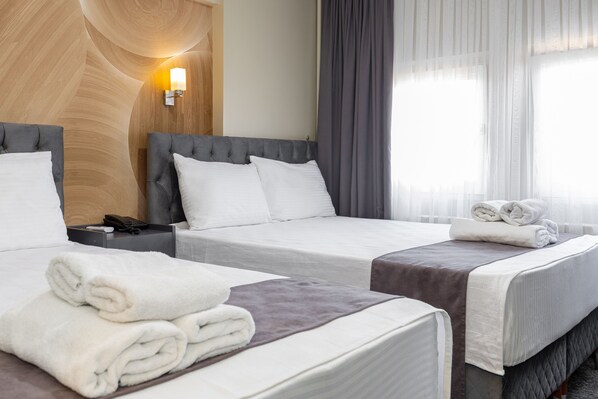 Habitación de hotel con dos camas, un revestimiento de madera, una lámpara de noche y una ventana con cortinas traslúcidas.