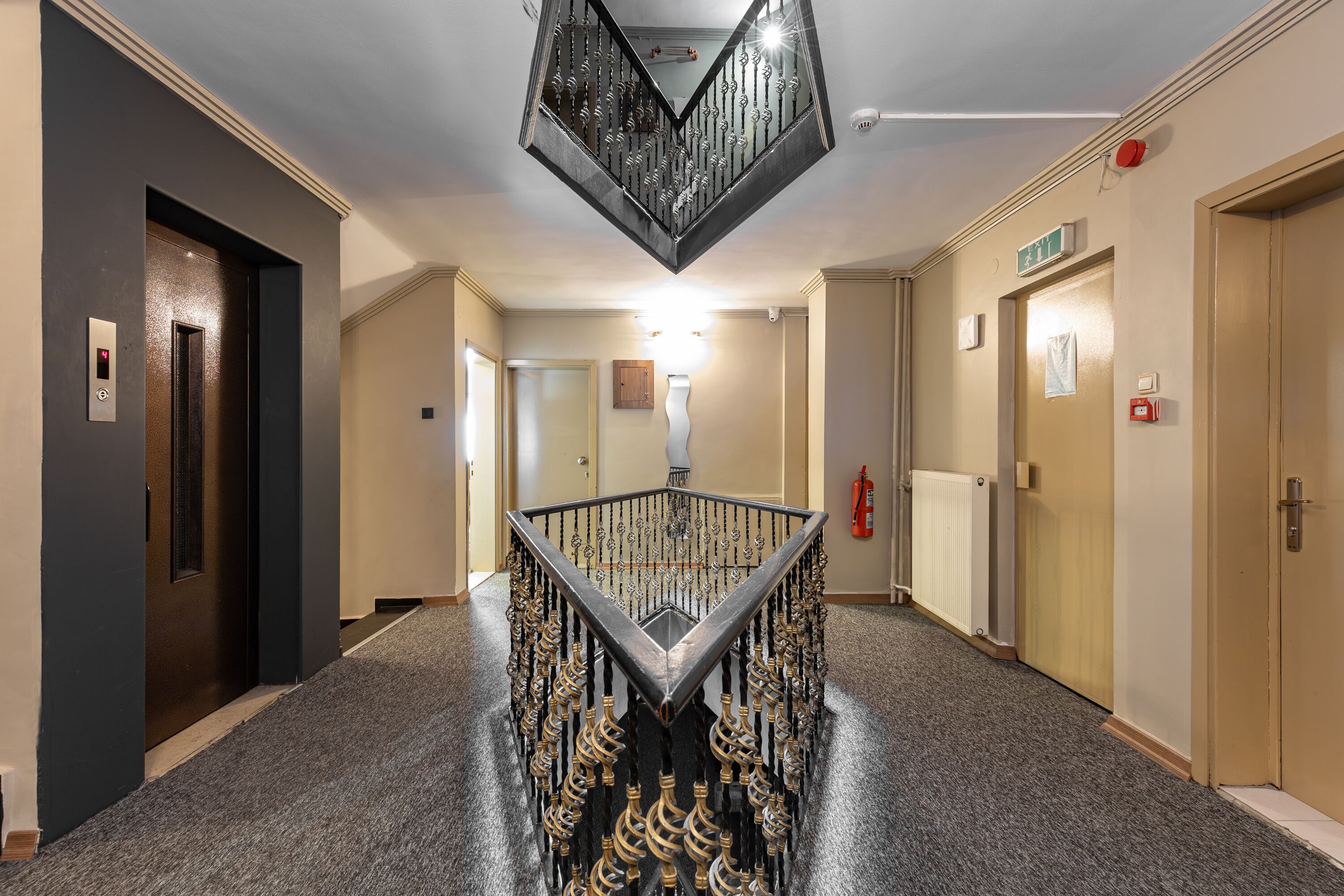 En moderne hotellobby med en central trappe, en receptionsdisk og en brandslukker på væggen.