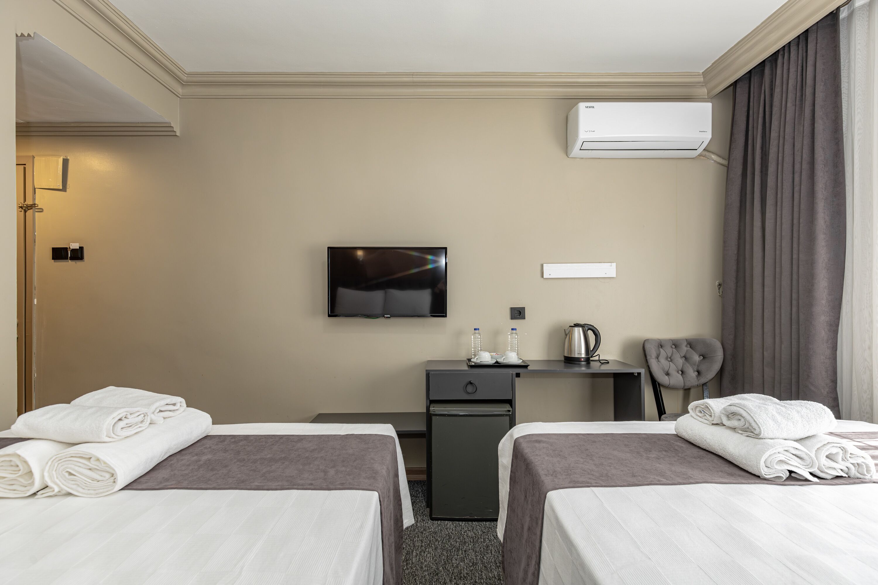 Habitación de hotel con dos camas, televisor, escritorio con silla y aire acondicionado.