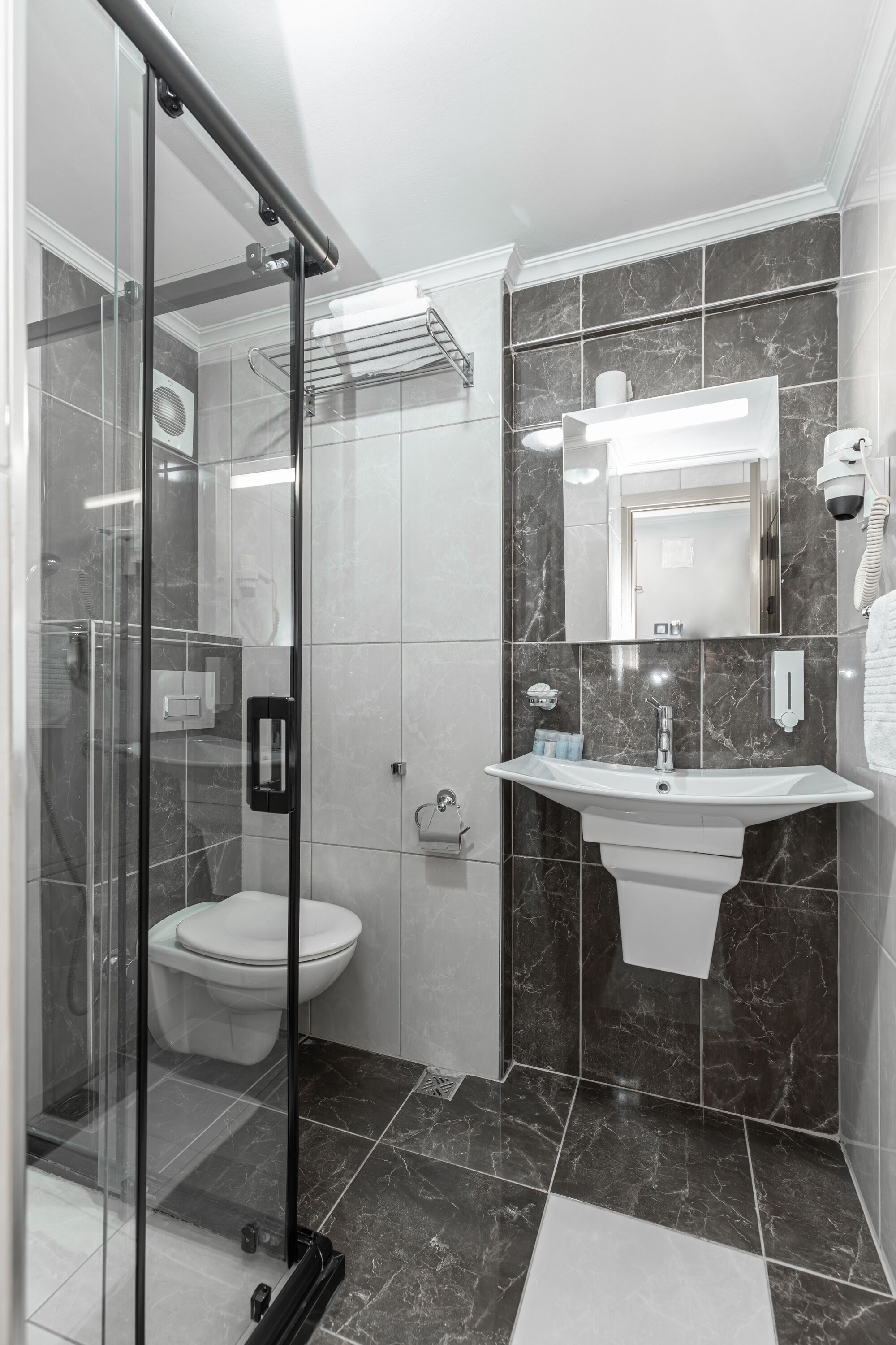 A modern bathroom with a glass shower enclosure, a white sink, and a marble-tiled wall.