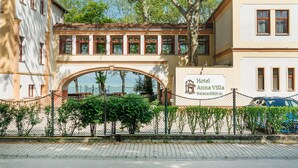 A hotel with a prominent archway entrance, a sign indicating it is Hotel Anna Villa, and a view of the sea in the background. - Hotel Anna Villa (Balatonfoldvar)