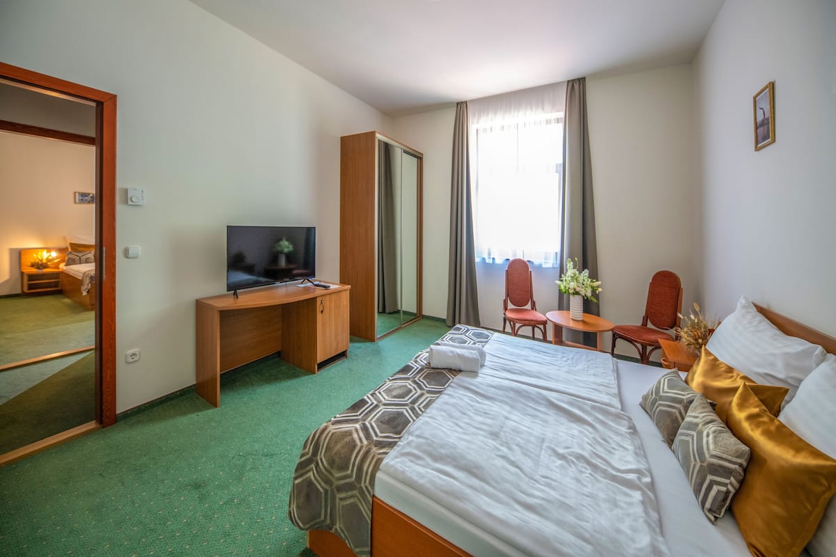 Ett hotellrum med en säng, ett skrivbord, en tv, en stol och ett fönster med gardiner.