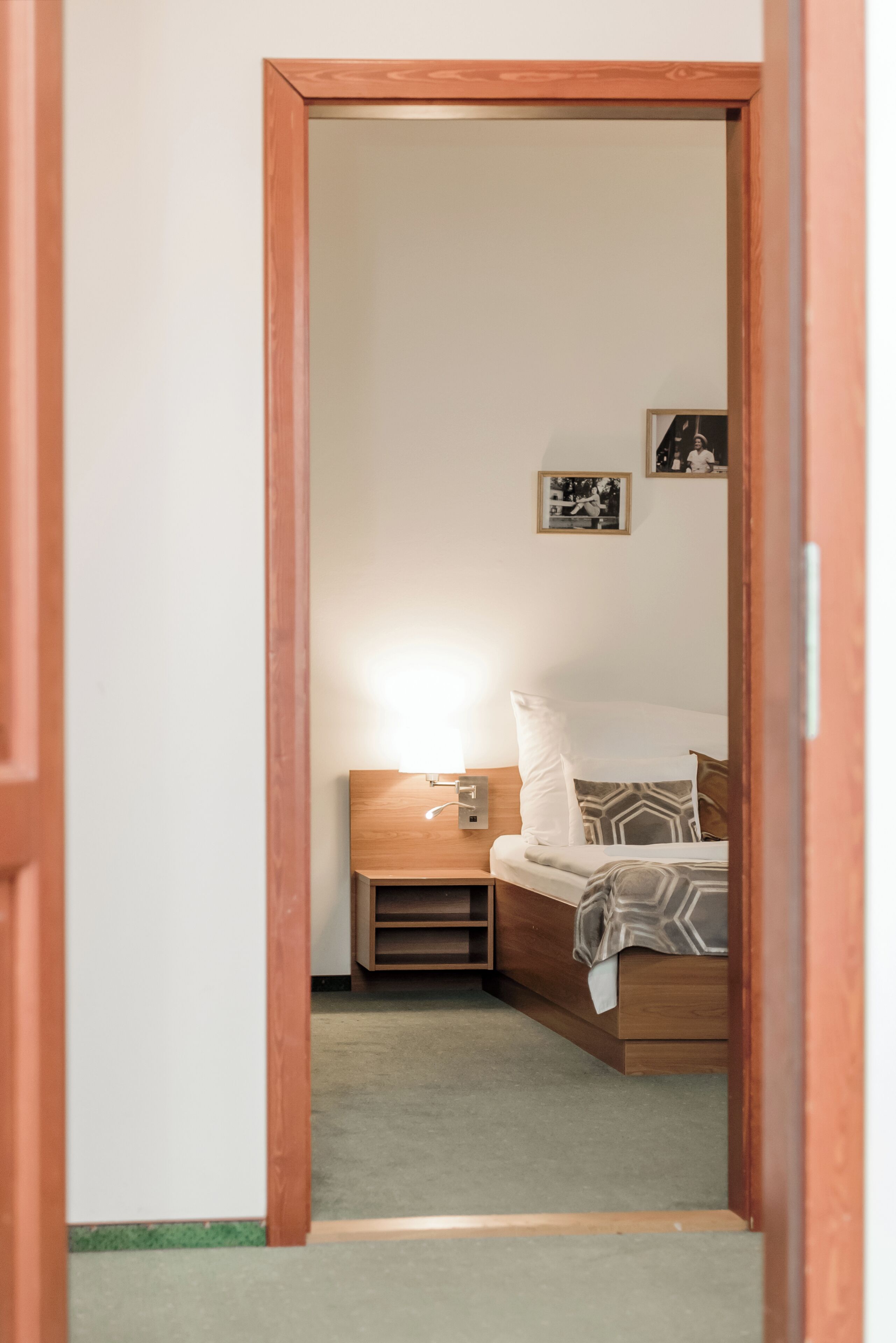 A bedroom with a wooden bed, a nightstand, and a wall-mounted light.