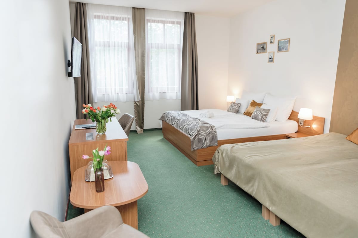 Ett hotellrum med en säng, ett skrivbord, en stol, ett litet bord med en vas med blommor och en tv som är monterad på väggen.