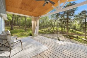A covered porch with a ceiling fan, a patterned sofa, and a view of a wooded area.