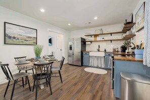 A modern kitchen with a dining area, wooden flooring, stainless steel appliances, and a view of the countryside.