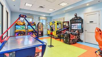Uma sala de jogos eletrônicos bem iluminada, com diversos jogos, incluindo um simulador de corrida e um jogo de boxe.