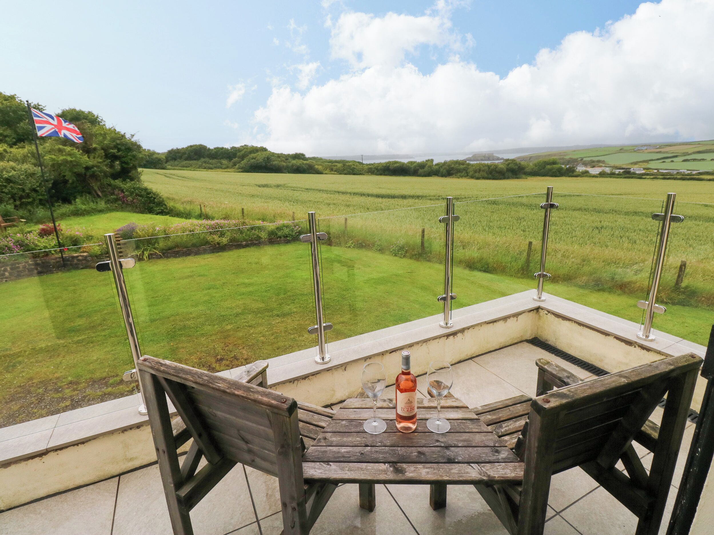 Eine Terrasse mit Tisch und Stühlen mit Blick auf ein grünes Feld und eine Flagge.